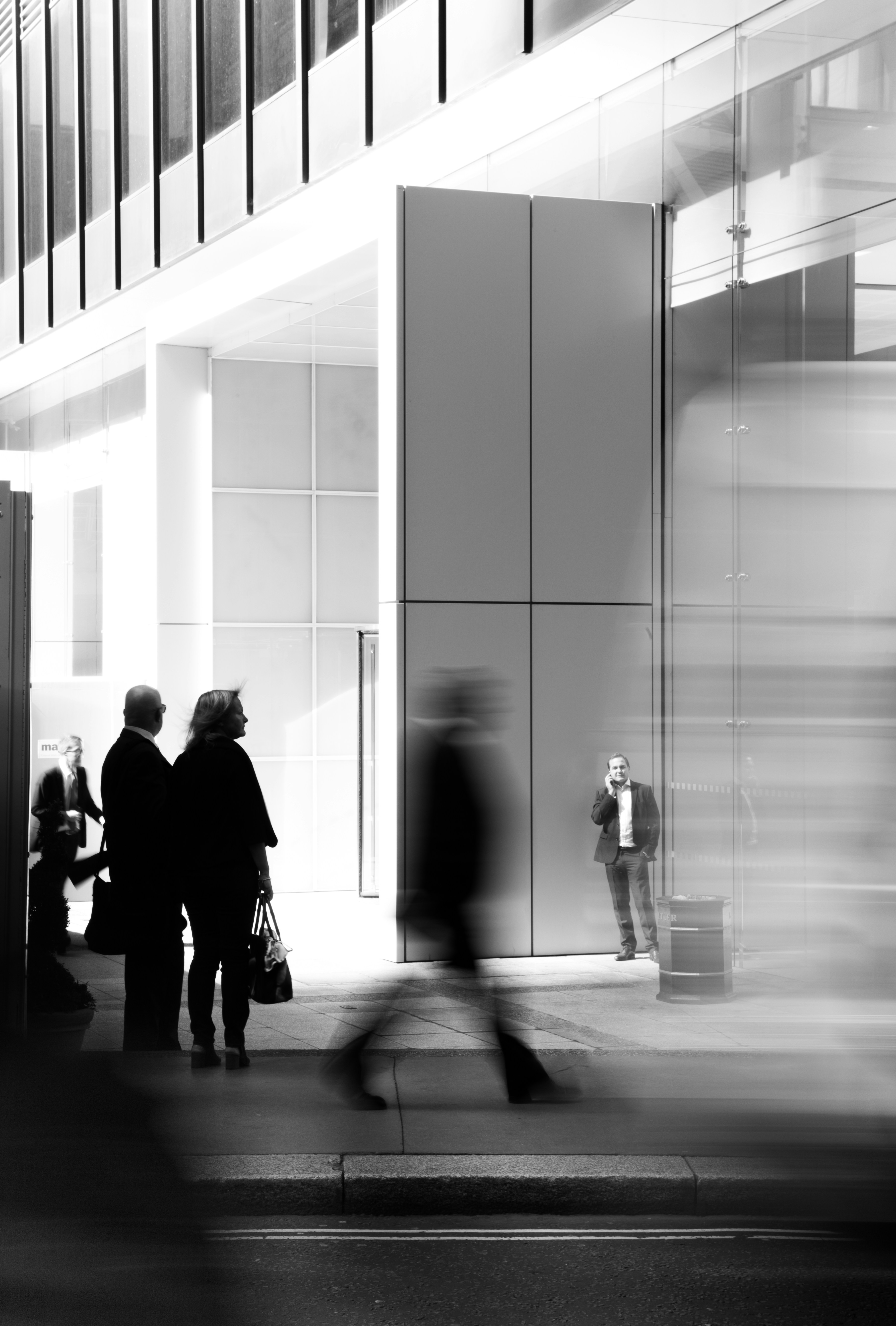 Figures walking through a modern glass-and-steel business district in black and white