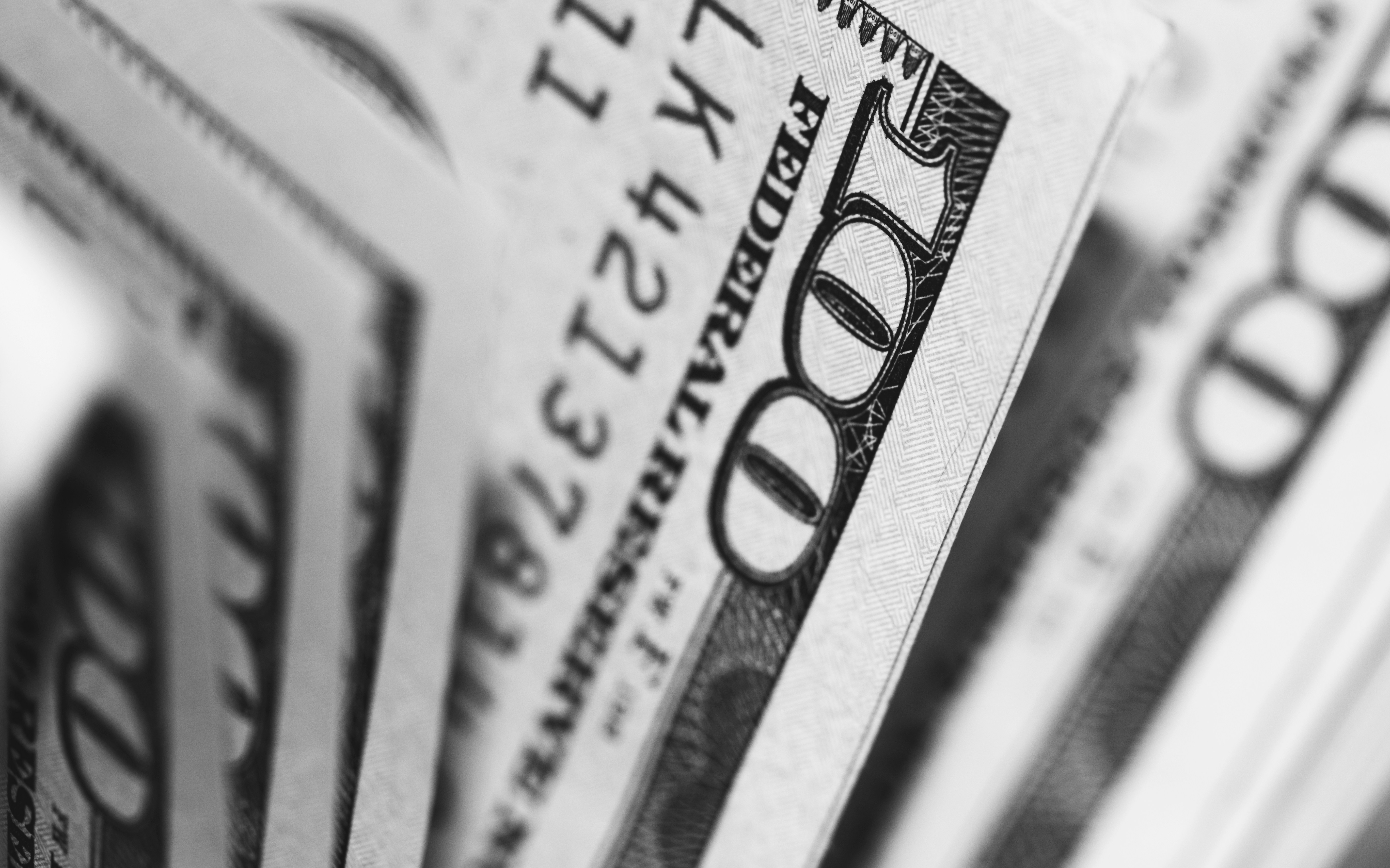 A close-up of fanned United States one-hundred-dollar banknotes in black and white
