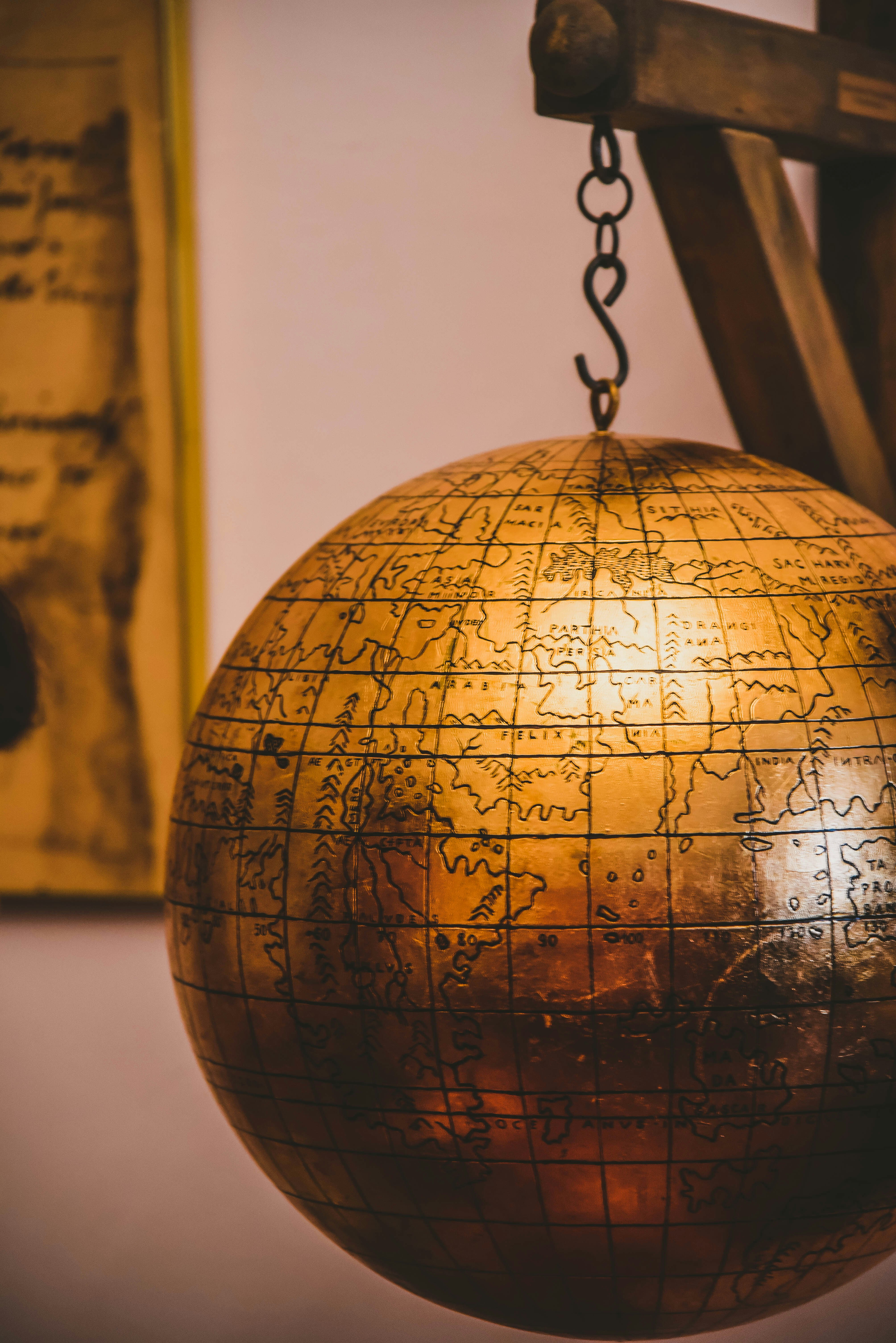 An antique brass world globe suspended on a chain against a muted backdrop